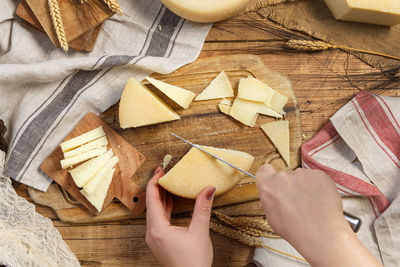 Hands cutting pieces of fresh homemade cheese on a wooden board top view