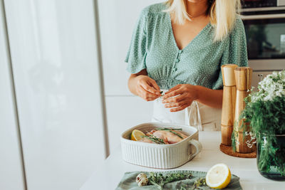 Midsection of a woman preparing chicken to roast at domestic kitchen