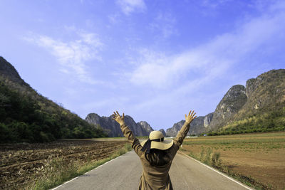 Rear view of woman with arms raised on mountain against sky