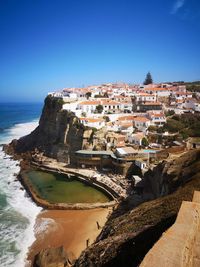 Buildings by sea against clear blue sky