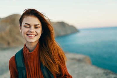 Portrait of smiling young woman standing at beach against sky