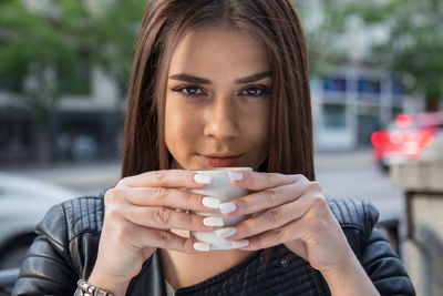 Close-up portrait of young woman drinking coffee at sidewalk cafe