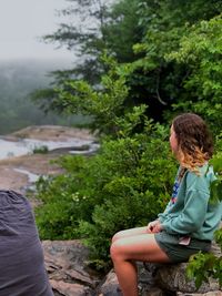 Side view of woman sitting on plant against trees