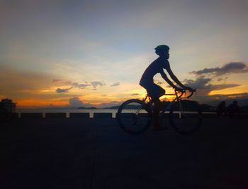 Silhouette man cycling by sea against sky during sunset