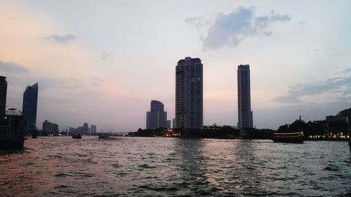 Sea by buildings against sky during sunset