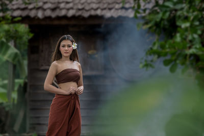 Portrait of young woman in traditional clothing standing against house