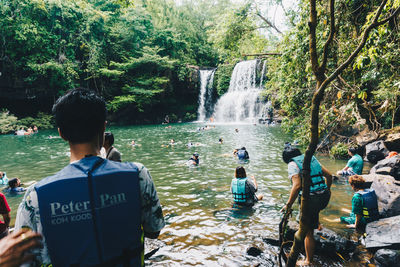 Rear view of people standing by river in forest