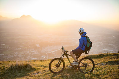 Side view of man riding bicycle on mountain against landscape during sunset