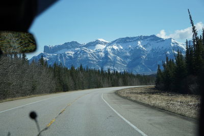 Road by mountains against clear sky during winter