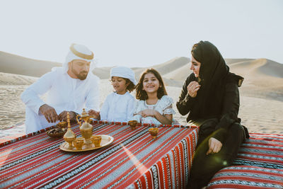 Happy family with tea on carpet at desert