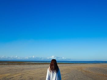 Rear view of woman standing at beach against blue sky