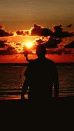 Rear view of silhouette man standing at beach during sunset