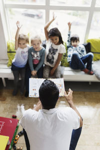 High angle view of male teacher asking questions to students at day care center