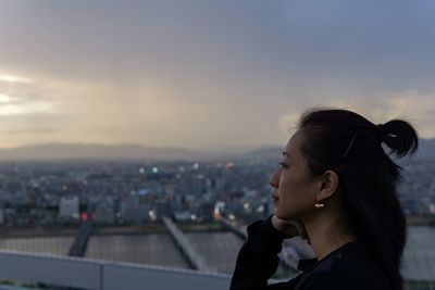 Portrait of woman looking at cityscape against sky