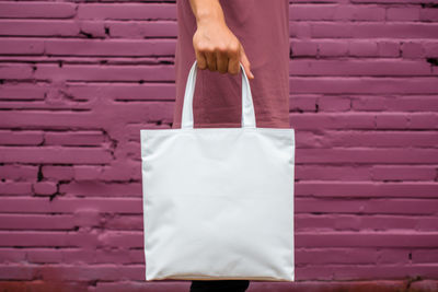 Cropped hand of woman holding shopping bags against brick wall