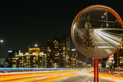 Light trails on road by buildings against sky at night