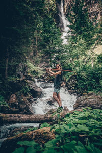 Full length of woman standing by stream in forest