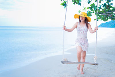 Young woman holding umbrella in sea against sky