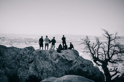 People on rocks by sea against clear sky