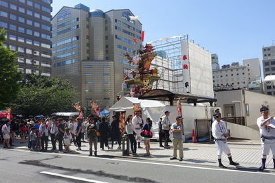 People on city street by buildings against sky