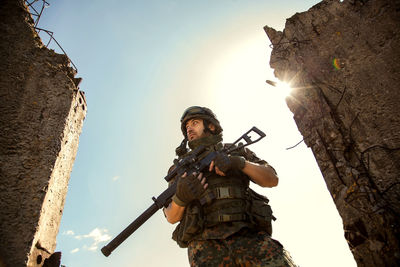 Young soldiers with guns, a soldier in equipment and with arms inspects a ruined house outside the