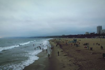 People on beach against cloudy sky