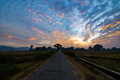 Road amidst field against sky during sunset