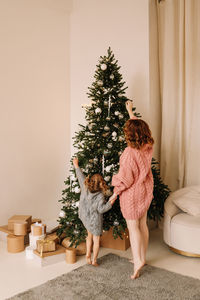 Happy mom and little daughter kid in sweaters hugging getting ready for  christmas holiday at home