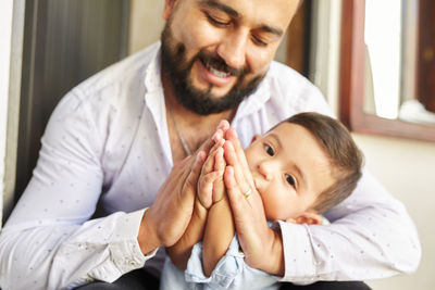 Hispanic father teaching cute toddler praying with clasped hands while sitting at home