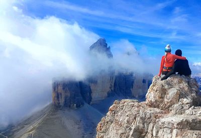 Rear view of people on rock by mountain against sky