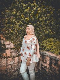 Full length portrait of young woman standing against trees