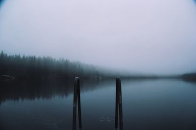 Close-up of railing by lake against sky during foggy weather