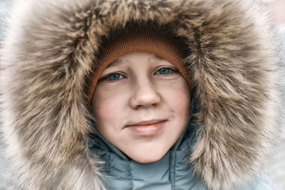 Close-up portrait of smiling white boy in hood winter snowy day happy child dressed in warm clothing