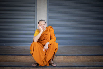 Full length of thoughtful monk sitting by closed shutter