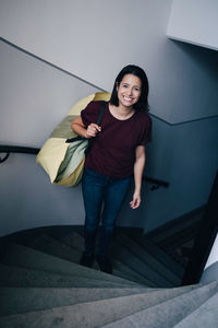 High angle portrait of smiling woman carrying bag while standing on steps