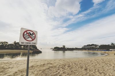 Information sign on beach against sky