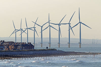 Windmills by sea against clear sky