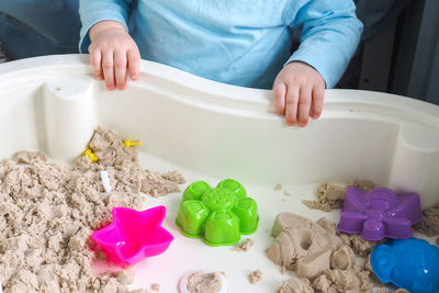 Faceless baby boy is playing with kinetic sand and colorful molds on the table