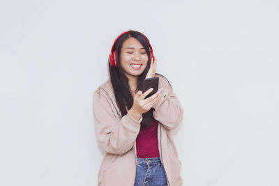 Young woman using phone while standing against white background