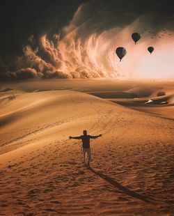 Rear view of man standing on sand against hot air balloons