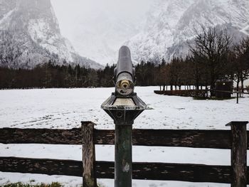 Coin-operated binoculars on snow covered field against mountains