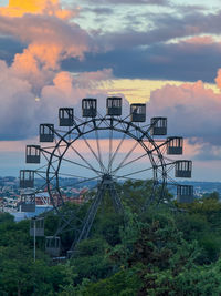 A ferris wheel with many small cabins on it. the sky is cloudy and the sun is setting