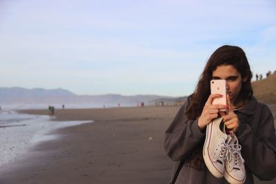 Portrait of young woman on beach against sky