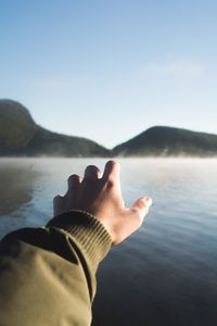 Low section of man by lake against sky