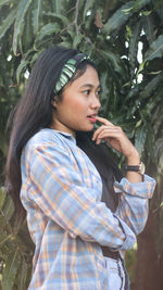 Young woman looking away while standing against plants