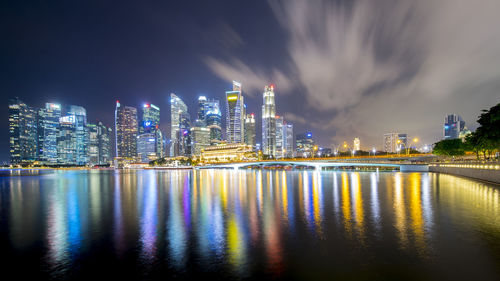 Illuminated buildings by river against sky at night