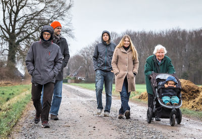 Multi-generation family in warm clothing walking on dirt road against sky