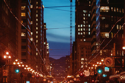 Illuminated street amidst buildings against sky at night