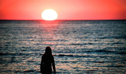 Silhouette woman by sea against sky during sunset