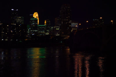 Illuminated city by river against sky at night